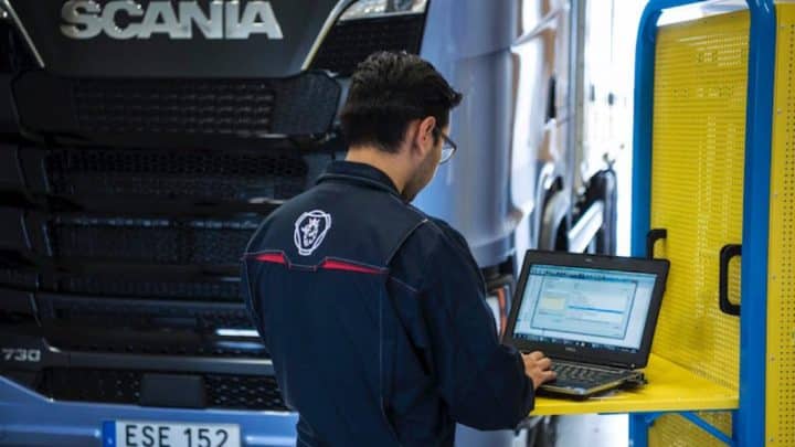 Working on a computer in front of a Scania lorry. Man arbetar på en dator framför en Scania-lastbil.