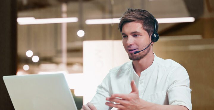A man is talking on a headset and looking at a computer. En man pratar i headset och ser på en dator.